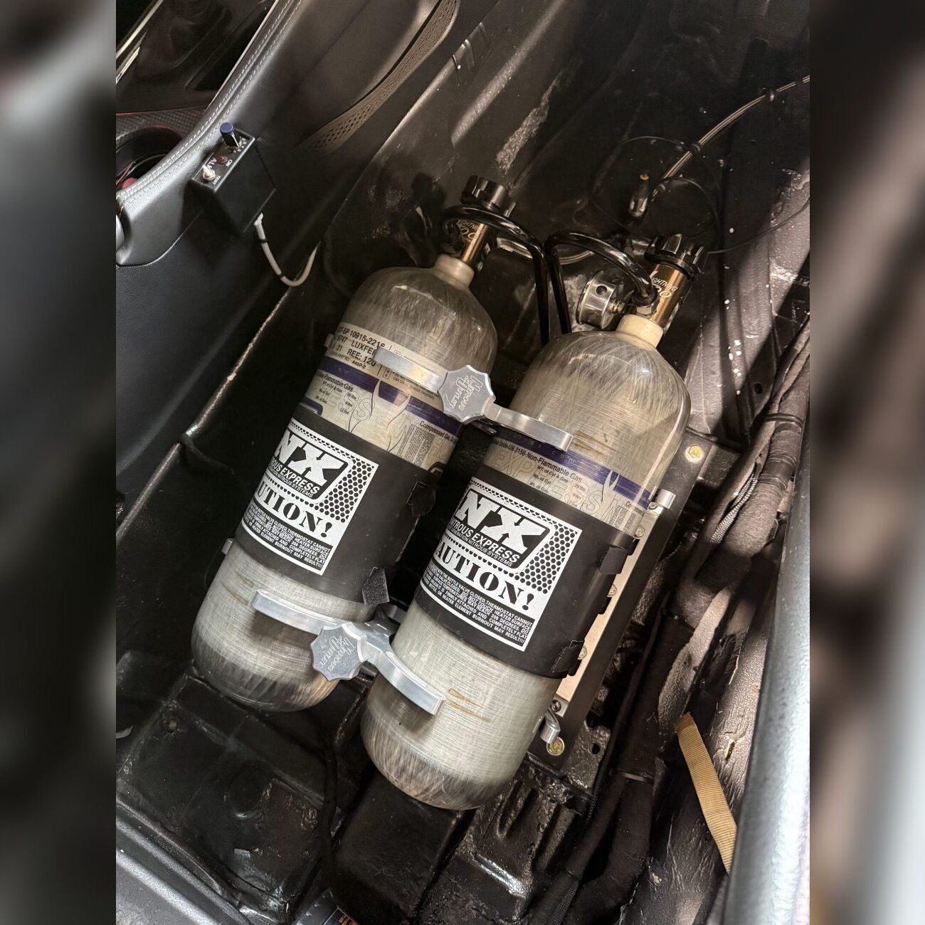 Two black and silver fire extinguishers mounted on a vehicle frame.