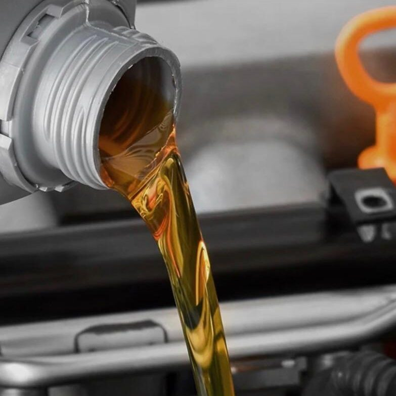 Motor oil being poured into a car engine compartment.